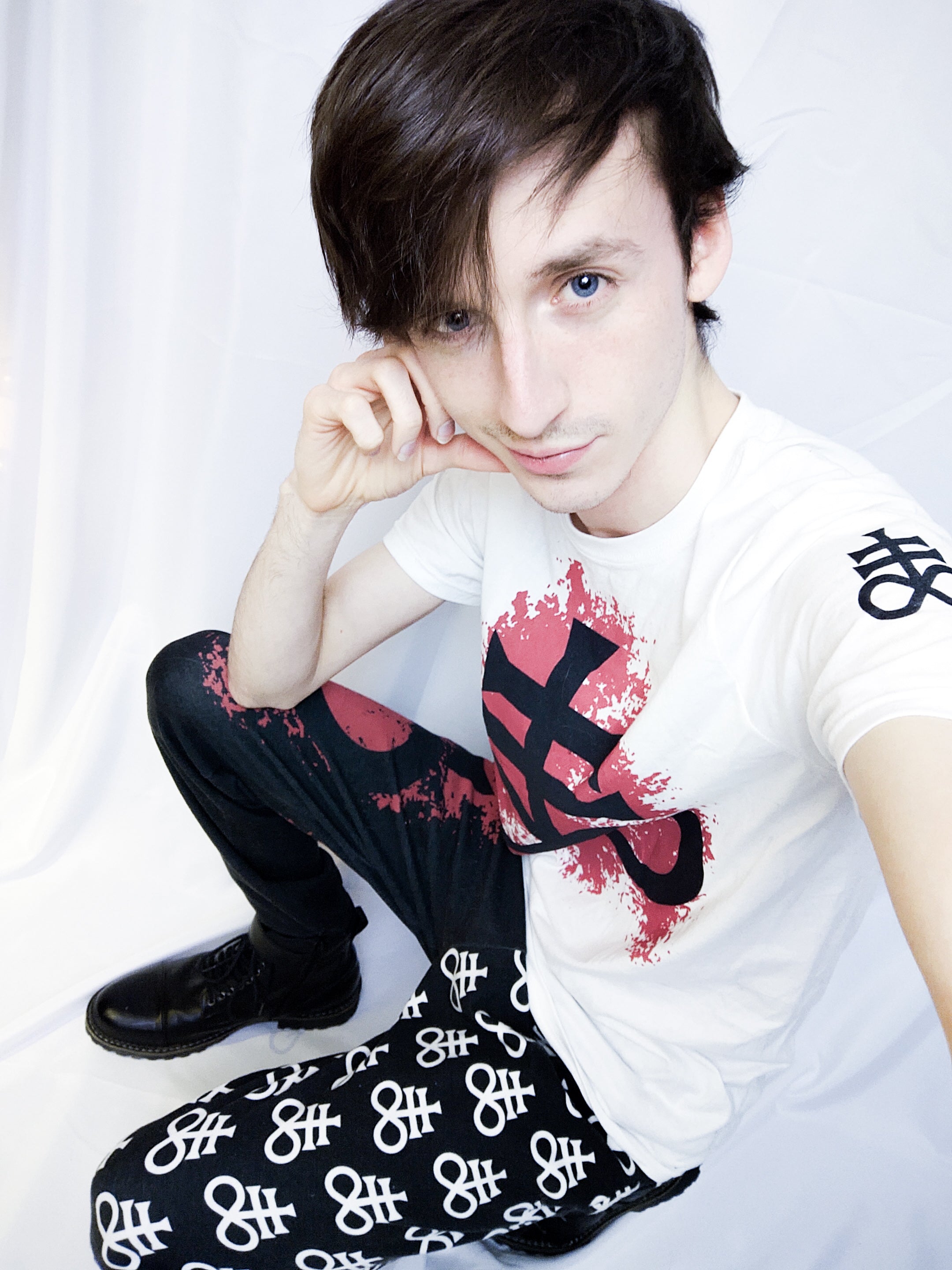 Joshua Roe modeling Luvicks Leviathan Cross matching set. A white T-shirt with a Leviathan cross design on a red splatter. Split design sweatpants with similar designs as the T-shirt