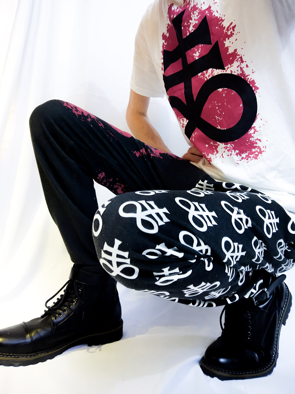 Joshua Roe modeling Luvicks Leviathan Cross matching set. A white T-shirt with a Leviathan cross design on a red splatter. Split design sweatpants with similar designs as the T-shirt